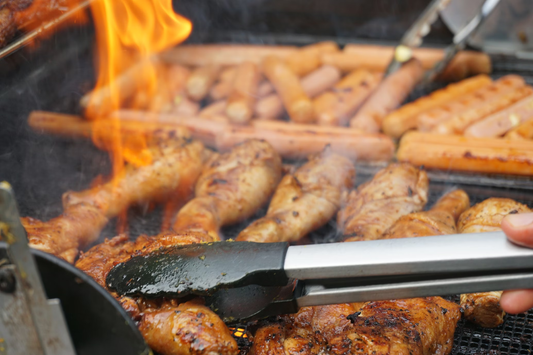 Sausages and hotdogs on a firey bbq with tongs flipping them