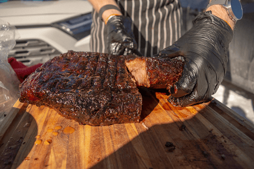 Man cutting brisket on a sunny table on a wooden cutting board