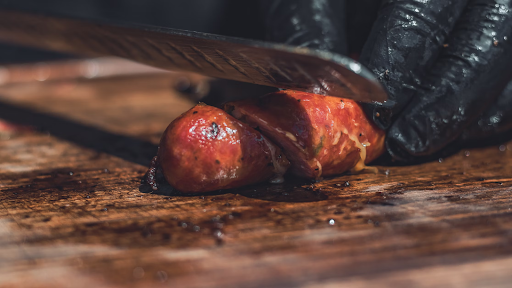 Image of someone at Truth BBQ cutting into a juicy sausage on a wooden cutting board.