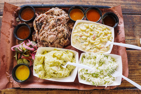 Image of TruthBBQ sides on a picnic bench. Pulled meat, mac and cheese, potatoes, and coleslaw.